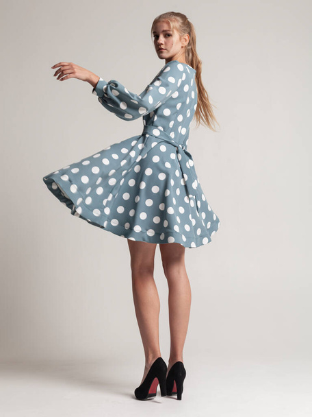 beautiful blonde in a blue dress with polka dots with long sleeves posing on a light background - Zdjęcie, obraz
