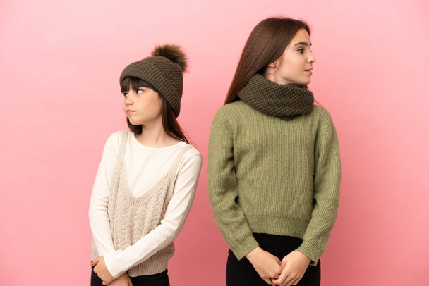 Petites sœurs portant des vêtements d'hiver isolés sur fond rose nerveux et effrayé - Photo, image