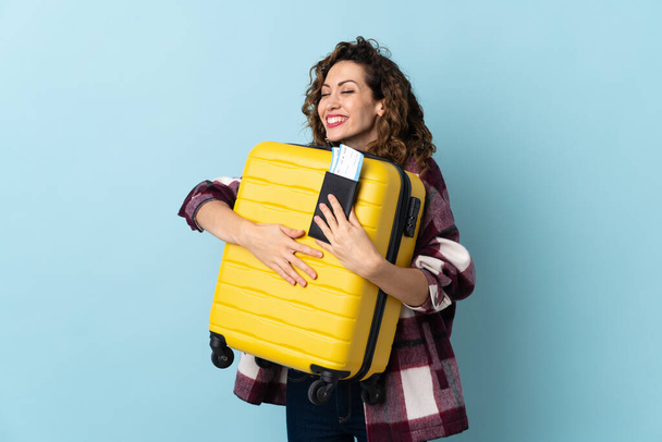 Young caucasian woman isolated on blue background in vacation with suitcase and passport - Photo, Image
