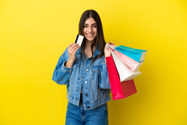 Mujer joven caucásica aislada sobre fondo azul sosteniendo bolsas de compras y una tarjeta de crédito - Foto, Imagen