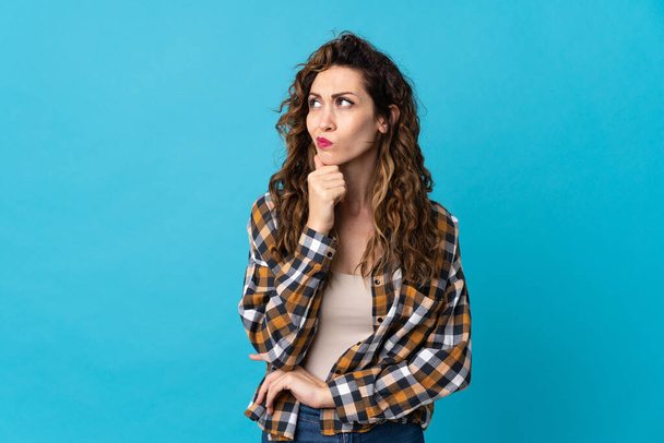 Young caucasian woman isolated on blue background having doubts and thinking - Foto, Bild