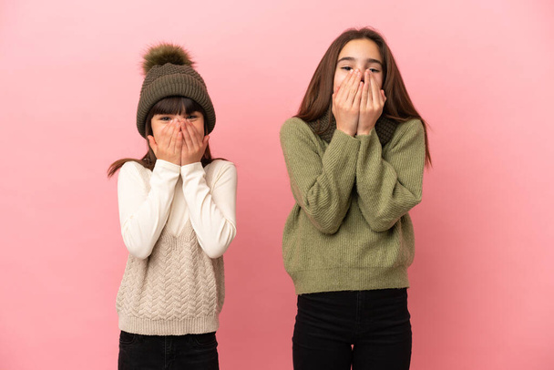 Little sisters wearing a winter clothes isolated on pink background smiling a lot while covering mouth - Photo, Image