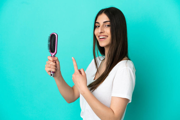 Young caucasian woman with hair comb isolated on blue background and pointing it - Photo, Image