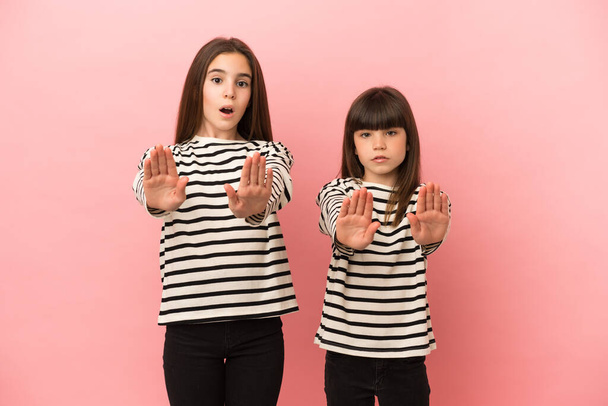 Kleine zusjes meisjes geïsoleerd op roze achtergrond maken stop gebaar voor teleurgesteld met een mening - Foto, afbeelding