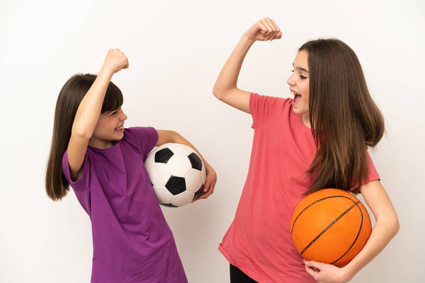 Piccole sorelle che giocano a calcio e basket isolate su sfondo bianco celebrano una vittoria nella posizione del vincitore - Foto, immagini