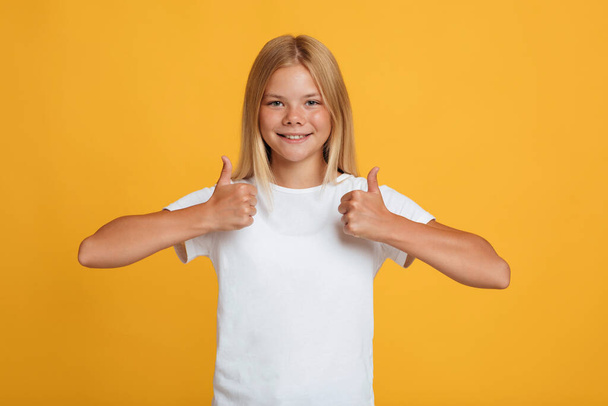 Joyeux adolescent intelligent élève blonde femme en t-shirt blanc montrant les pouces geste - Photo, image