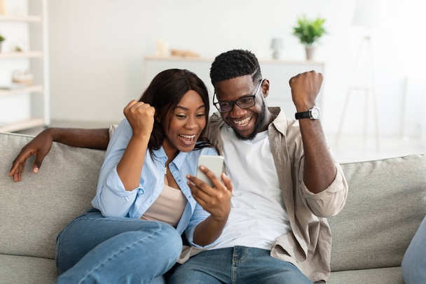 Αφροαμερικανοί ζευγάρι που χρησιμοποιούν κινητό τηλέφωνο, γιορτάζοντας νίκη - Φωτογραφία, εικόνα