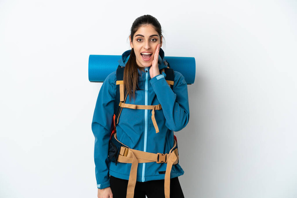 Молодой альпинист с большим рюкзаком на изолированном фоне с удивлением и шокированным выражением лица - Фото, изображение