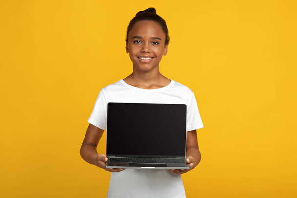 Smiling pretty teen african american pupil lady in white t-shirt hold laptop with blank screen - 写真・画像