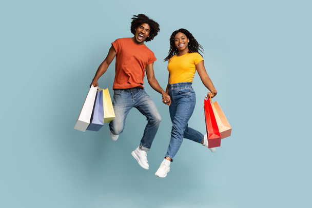 Emotional black couple with shopping bags jumping up - Fotó, kép