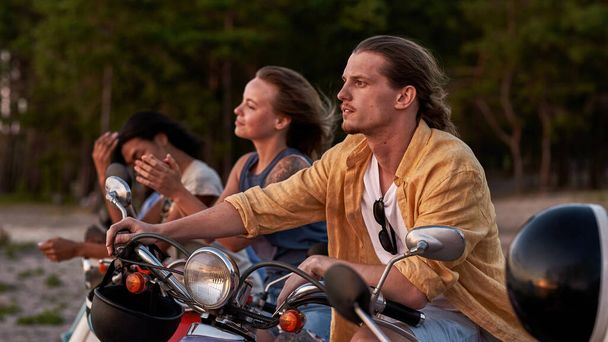 Caucasian young guy, motorcycle rider looking away, spending time together with his friends outside the city - 写真・画像