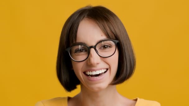 陽気な若いブルネットの女性が黄色のスタジオの背景にポーズを微笑む - 映像、動画