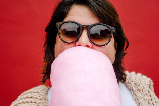 gros plan d'une femme avec des lunettes sombres mord un coton de sucre rose porte des lunettes sombres - Photo, image