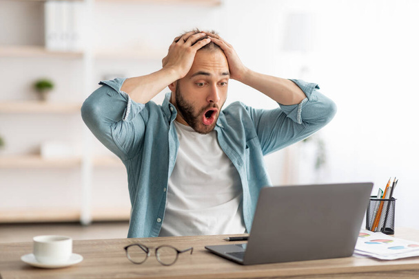 Rettegett férfi szabadúszó laptopot néz, megragadja a fejét, hibát vét az üzleti projektben, lekési a határidőt otthon - Fotó, kép