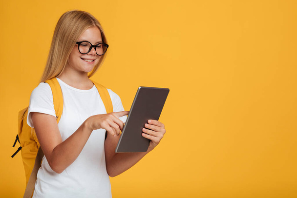 Usmívající se dospívající běloška v bílém tričku, brýle s batohem studie s tabletou - Fotografie, Obrázek