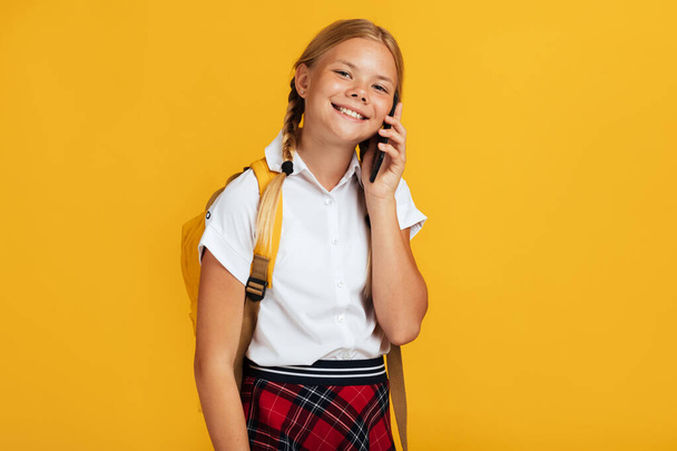 Smiling teenager caucasian blonde female with pigtails, backpack speaks by phone - Fotó, kép