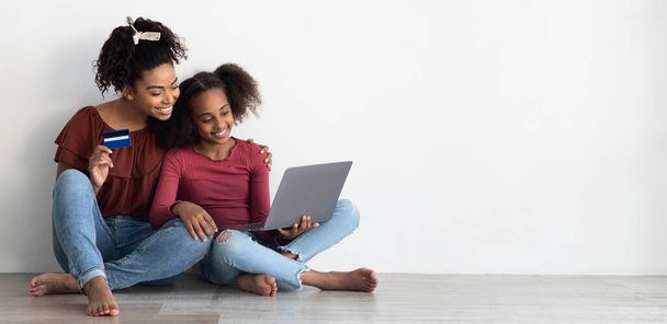 Весела афро-американська мати і підліток купують щось в інтернеті. - Фото, зображення