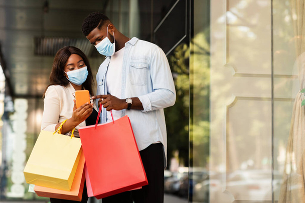 Retrato de casal negro usando celular usando máscaras perto do shopping - Foto, Imagem