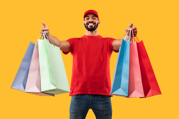 Middle-Eastern Male Courier Giving Shopper Bags Delivering Clothes, Yellow Background - Foto, Imagem