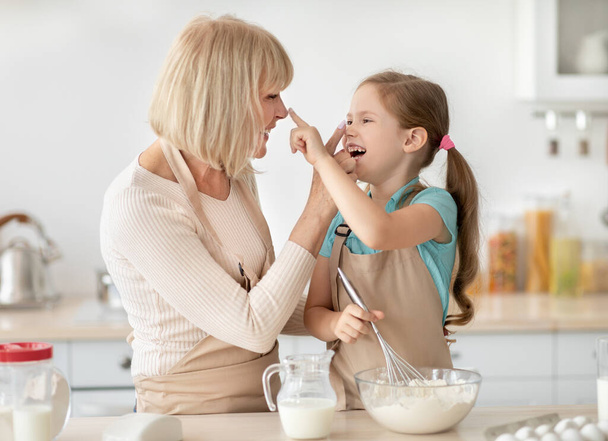 Mulher madura e menina cozinhar brincando com farinha tocando narizes - Foto, Imagem