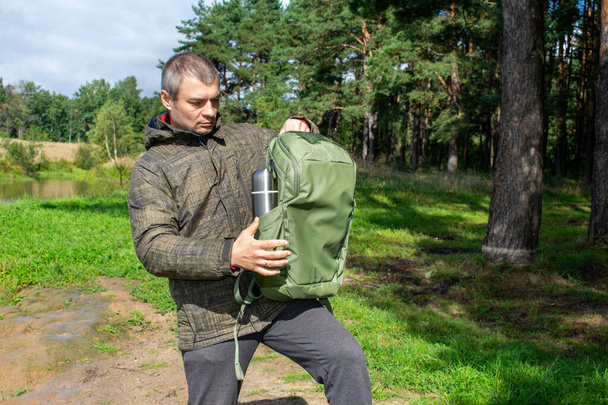 Egy férfi zöld hátizsákkal és egy fém termosz teával vagy kávéval sétál az erdőben sétálni. Turista vakáción. Egyedül túrázni. Kempingezés. - Fotó, kép