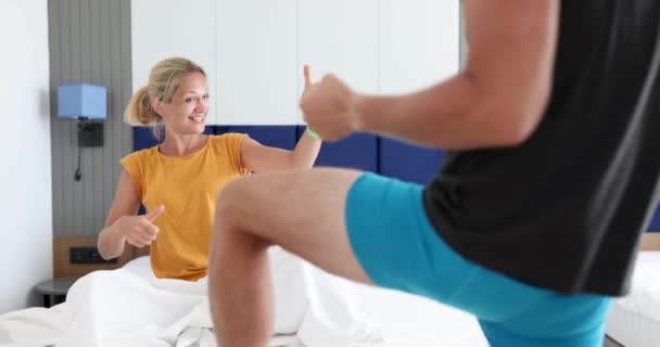 Mujer alegre mira al hombre en pantalones cortos bailando en el dormitorio 4k película - Imágenes, Vídeo