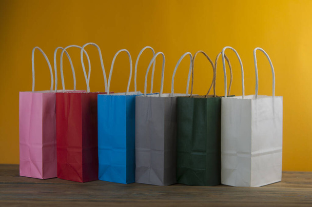 Minimales Online-Shopping-Konzept, bunte Einkaufstasche aus Papier auf gelbem Hintergrund für Kopierraum. Kunde kann alles von zu Hause aus kaufen und der Bote wird liefern. - Foto, Bild