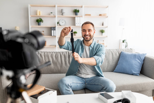 Freundlicher männlicher Blogger dreht Videobewertung des neuen Smartwatch-Modells mit professioneller Kamera zu Hause - Foto, Bild