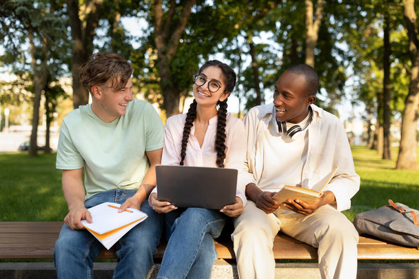 Divers étudiants amis apprennent assis sur le banc, en utilisant un ordinateur portable à l'extérieur sur le campus universitaire - Photo, image