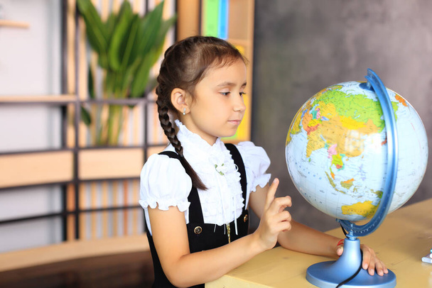 Portret van een meisje in een schooluniform met een wereldbol in haar handen. - Foto, afbeelding