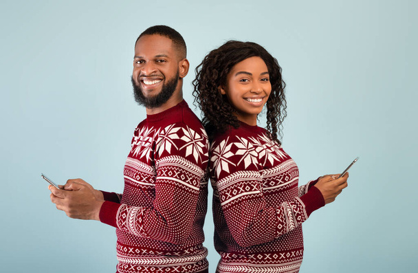 Nieuwjaar en Kerstmis promoties. Gelukkig Afrikaans amerikaanse man en vrouw met smartphones en een back-to-back - Foto, afbeelding