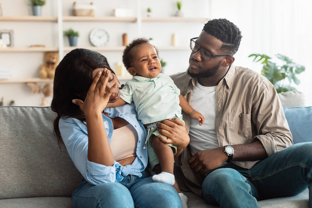 Tired black parents sitting with crying kid on sofa - Photo, Image
