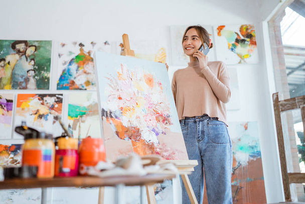 занятой художник, стоящий рядом с ее картиной, пока она звонит по телефону - Фото, изображение