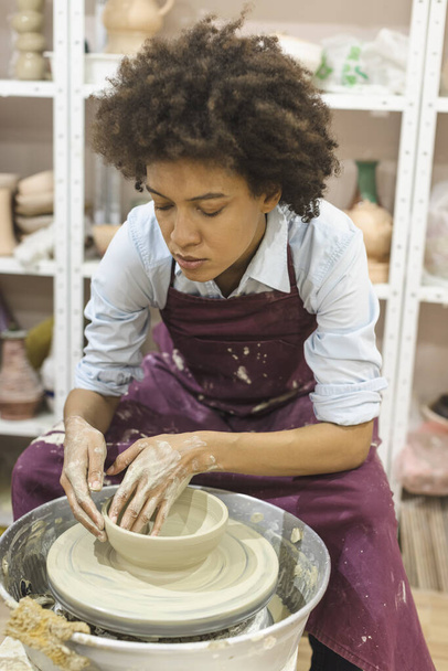 Creative afro american young woman molding clay on pottery wheel. Workshop in ceramic studio. Female artist.  - Photo, Image