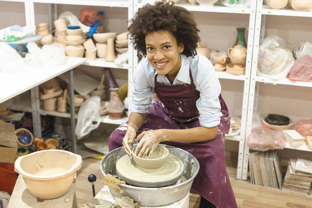 陶器の車輪の上に粘土を成形する創造的なアフロアメリカの若い女性。セラミックスタジオでのワークショップ。女性アーティスト.  - 写真・画像