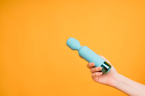A womans hand holds a blue dildo or vibrator for sex on a yellow background.Useful for a sex shop - Фото, изображение