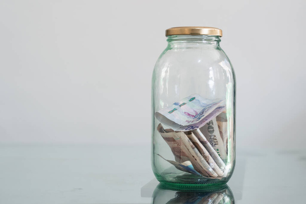 money, Colombian banknotes in glass jar, on glass table, financial, savings. Money box, jar full of cash, concept of saving money, planning and controlling expenses, space for text. economy concept. - Photo, image