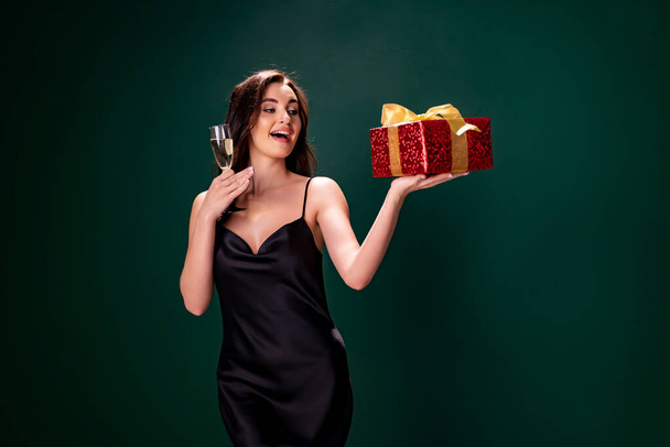 woman in black dress holds the gift red box and glass of champagne. Party time. Holiday concept - Фото, зображення