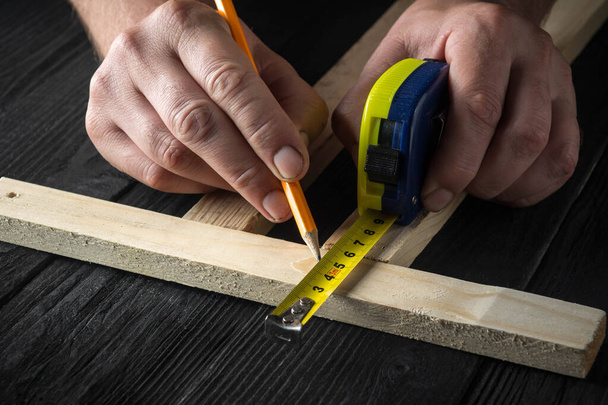 El carpintero hace marcas de lápiz en un bloque de madera. Las manos del maestro de cerca en el trabajo. Ambiente de trabajo en un taller de carpintería - Foto, Imagen