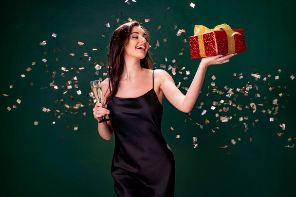 Excited woman in black dress holds the gift red box and glass of champagne. Party time. Holiday concept - Фото, изображение