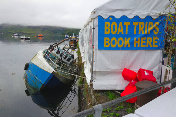 Señal divertida 'excursiones en barco - reservar aquí' en el puerto de Portree, Skye  - Foto, imagen