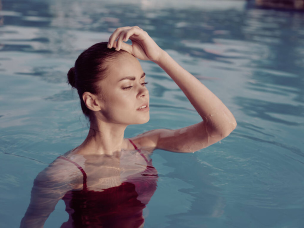 mooie vrouw in een rood badpak in het zwembad houdt haar hand op haar hoofd close-up - Foto, afbeelding
