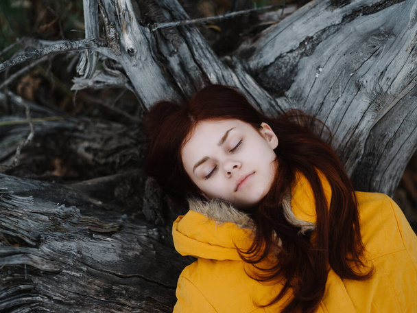 mulher bonita em uma jaqueta amarela encontra-se em uma árvore no descanso da floresta - Foto, Imagem