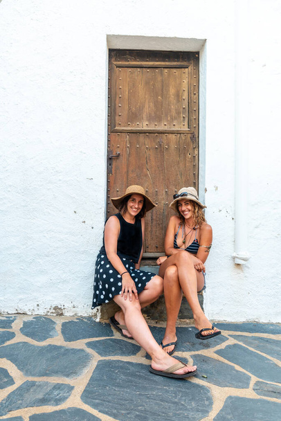 Girlfriends in summer enjoying the holidays. Caucasian girls sitting by a door enjoying the heat on vacation - 写真・画像