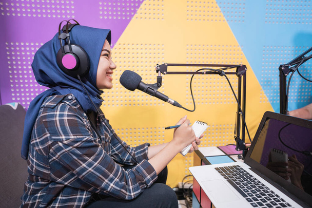 excited muslim woman is recording a podcast in studio with laptop - Foto, afbeelding
