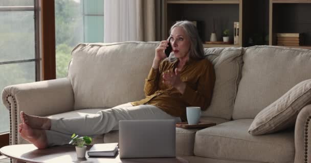 Aged woman relax on sofa holds cellphone make personal call - Πλάνα, βίντεο