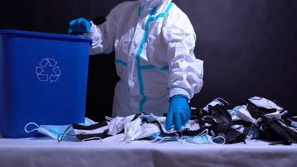 Recycle worker in gloves, sorting medical masks in the recycle bin. Depiction of recycle plant facility. Pollution by surgical masks in coronavirus pandemic and harm to environment. Disposable masks. - Foto, Imagen
