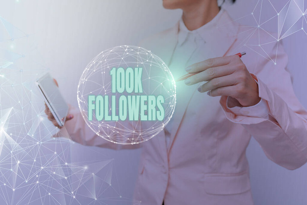Χειρόγραφο κείμενο 100K Followers. Επιχειρηματικός αριθμός ιδέα των ατόμων που ακολουθεί κάποιος στο Instagram Γυναίκα με κοστούμι κρατώντας tablet με κυκλική ολογραφική οθόνη. - Φωτογραφία, εικόνα
