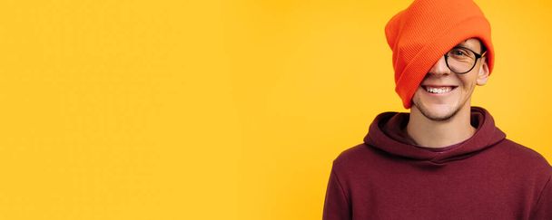 handsome man puts on an orange hat on the floor of his face, porter of a cheerful positive smiling man, on a yellow background, concept: autumn or winter insulation, clothes for cold weather - Foto, imagen