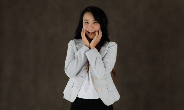 Wesoły młody Azji kobieta w stylowe formalne ubrania śmiejąc się szczęśliwie podczas zabawy na ciemnoszarym tle - Zdjęcie, obraz